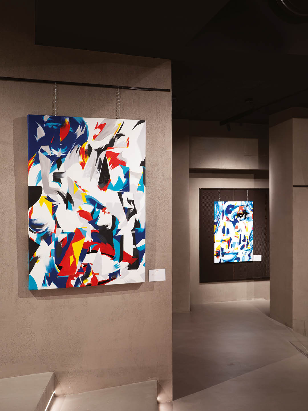 Two colorful abstract paintings by DutyGorn displayed in the Momentum exhibition at Kruso Art in Milan, featuring dynamic geometric shapes and bold brushstrokes.