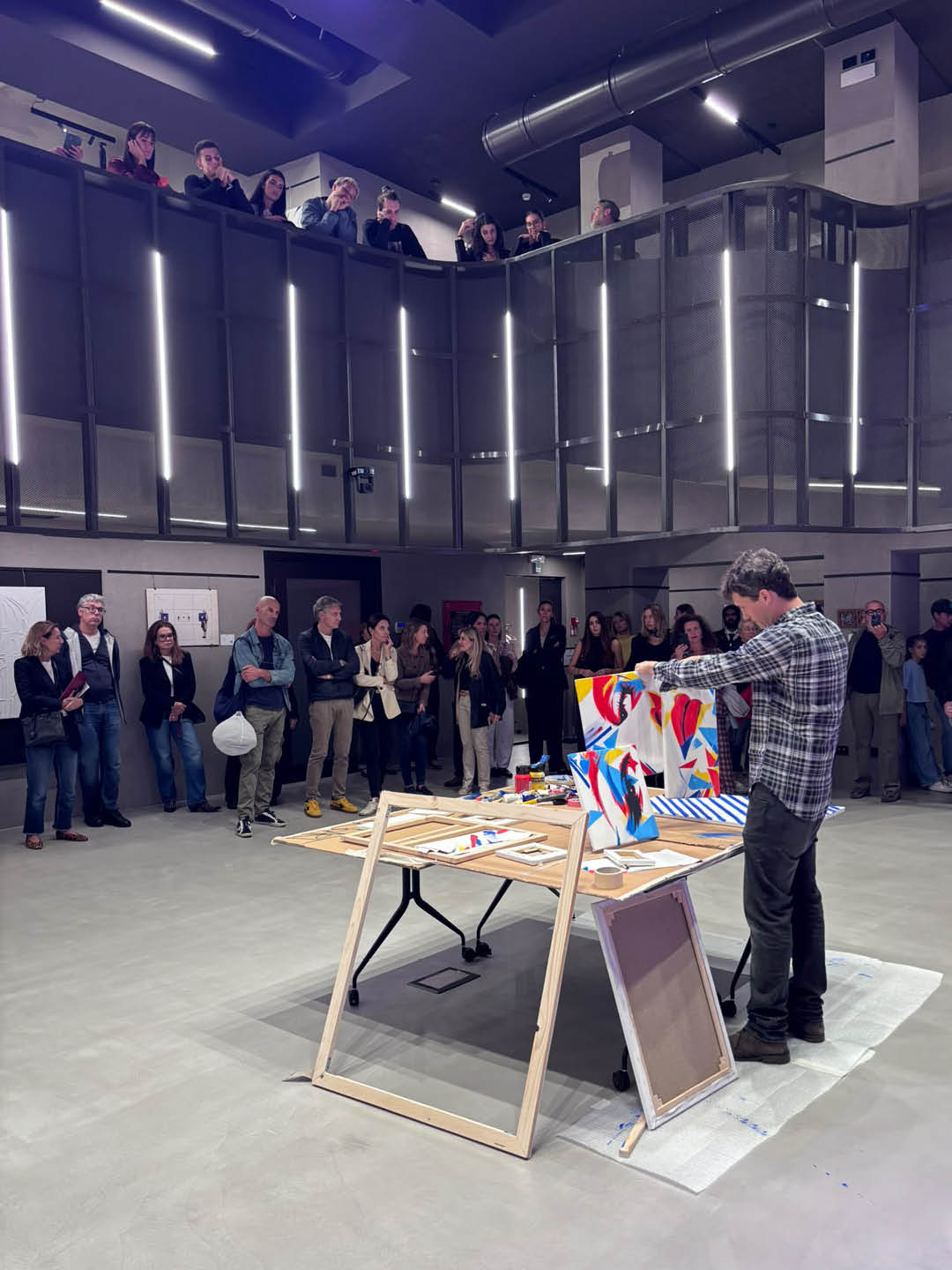 Guido DutyGorn reconstructing a colorful polyptych during a live art performance, surrounded by visitors watching from the gallery floor and upper balcony.