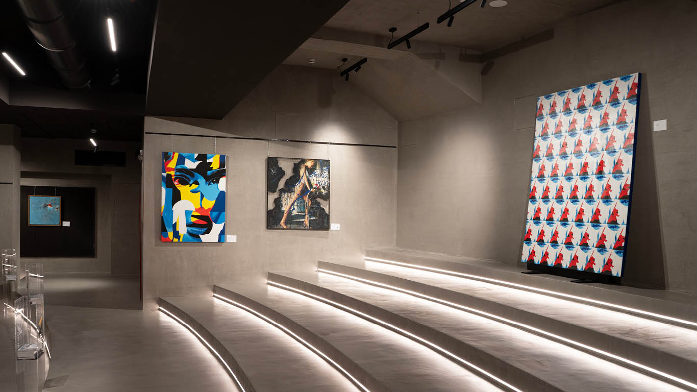 Exhibition installation featuring contemporary artworks by DutyGorn and other artists at Kruso Art in Milan, with illuminated steps and paintings displayed on dark walls.