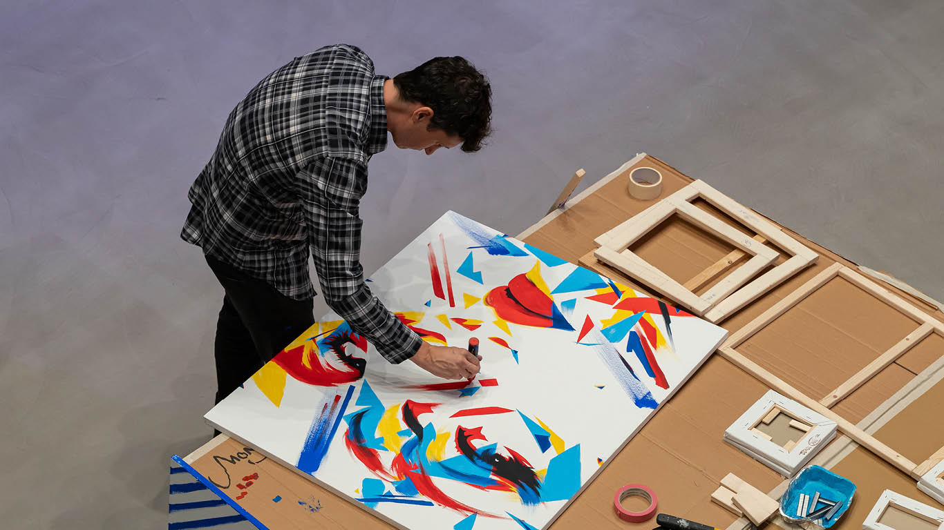 Guido DutyGorn working on a colorful portrait composed of multiple canvas panels during a live art performance, viewed from above.